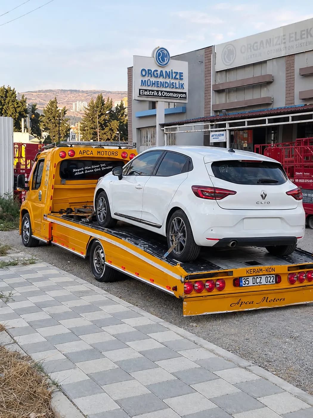Servis önünde sarı platform çekiciye yüklenmiş beyaz SUV