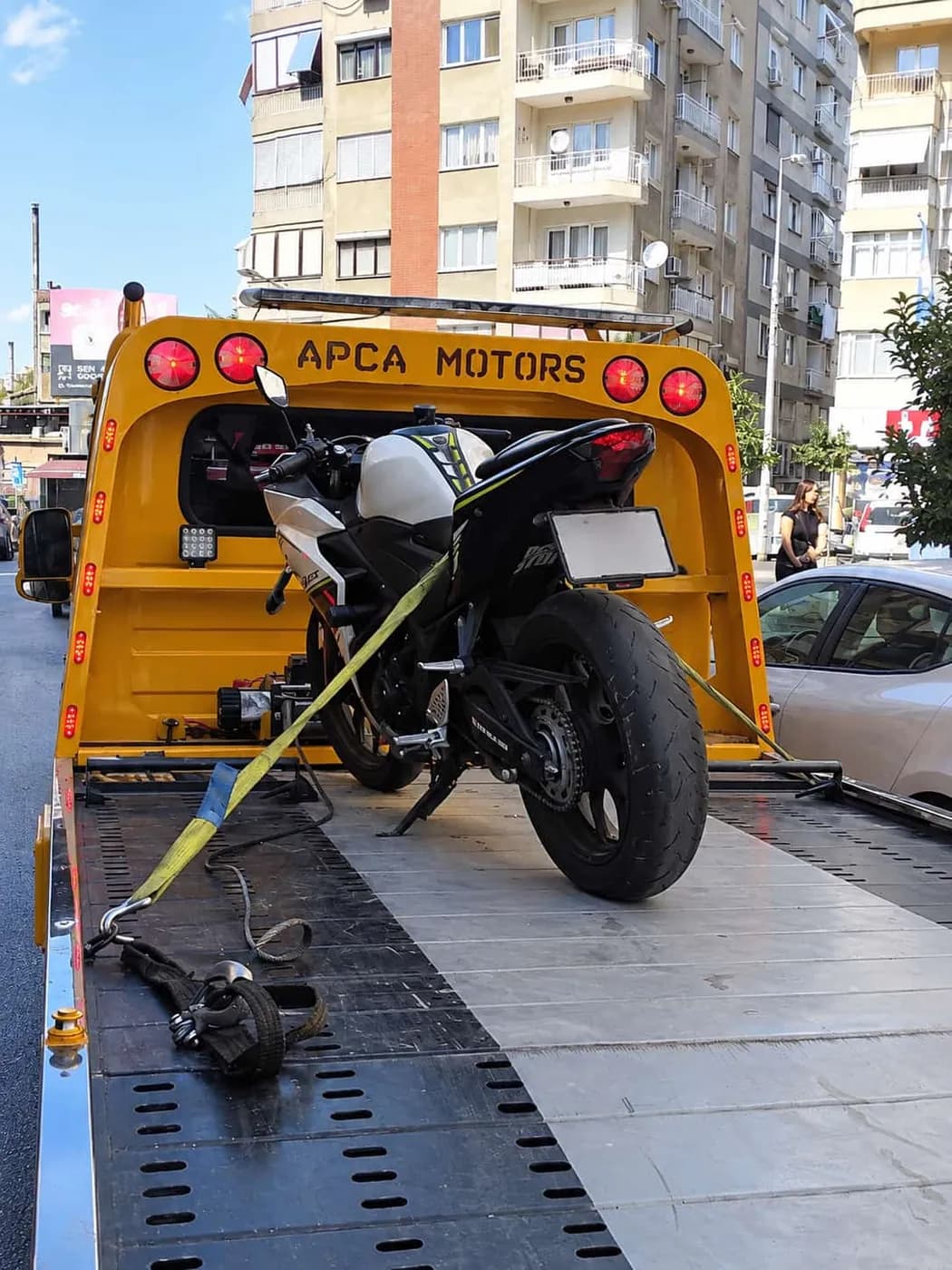 Bağlama kayışlarıyla sarı platform çekiciye sabitlenmiş motosiklet